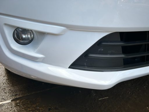 Close-up of a car's front bumper with fog light and grille details.