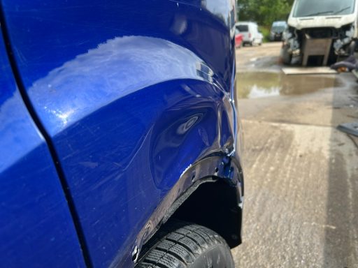 Close-up of a blue car displaying a dent on the rear fender.