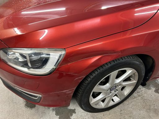 Close-up of a red car's front left side, highlighting the wheel and headlight.