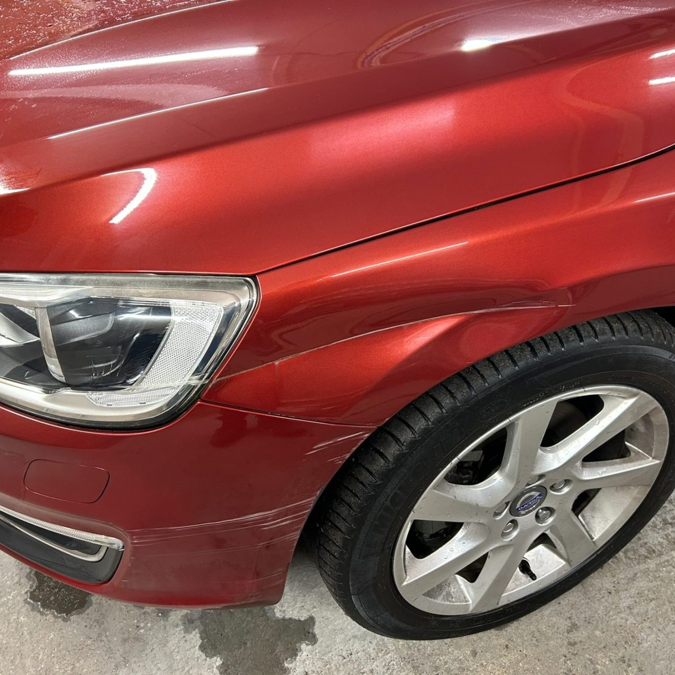 Before Red car with a scratched front panel and a silver alloy wheel.