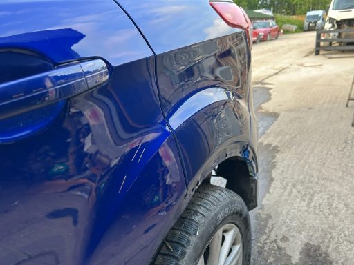 Close-up view of a blue car's rear wheel arch showing minor damage.