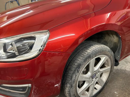 Close-up of a red car's front wheel and fender with some dirt and minor scratches.