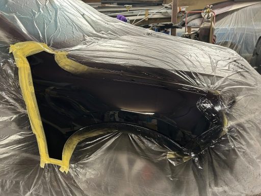 A car part covered in plastic sheeting, prepared for painting.